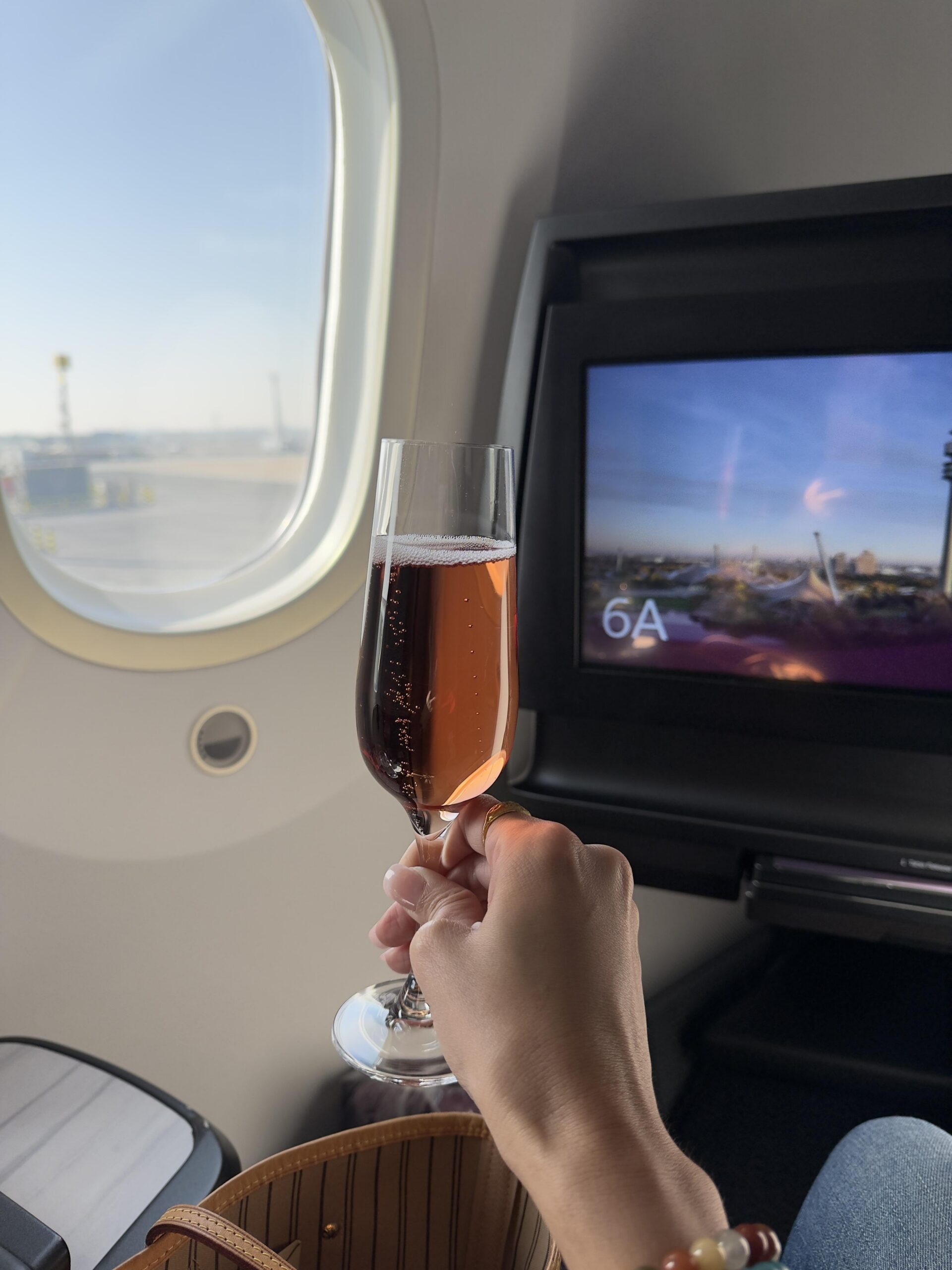 Rosé-Champagner im Glas vor einem Flugzeugfenster bei Sonnenschein – luxuriöser Reisemoment