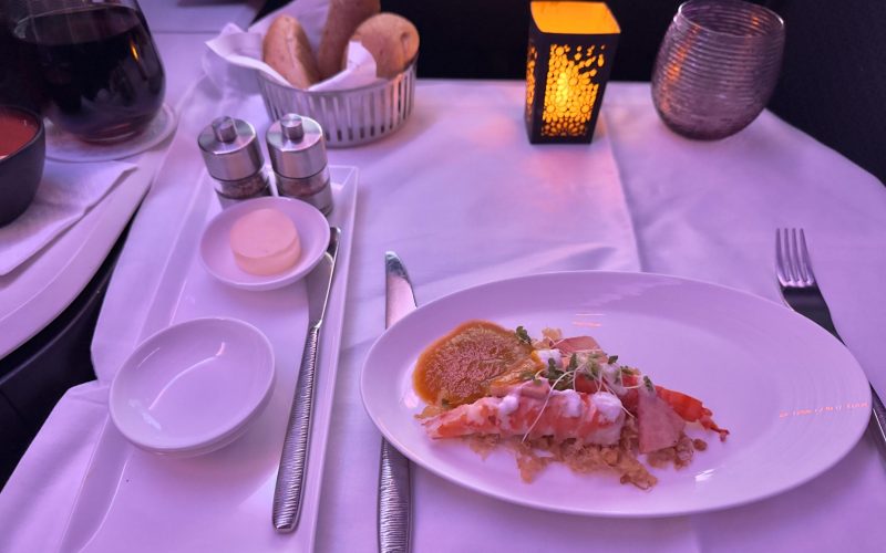 Luxuriös serviertes Hummergericht mit Kokosflocken und Brot in der Business Class eines Flugzeugs