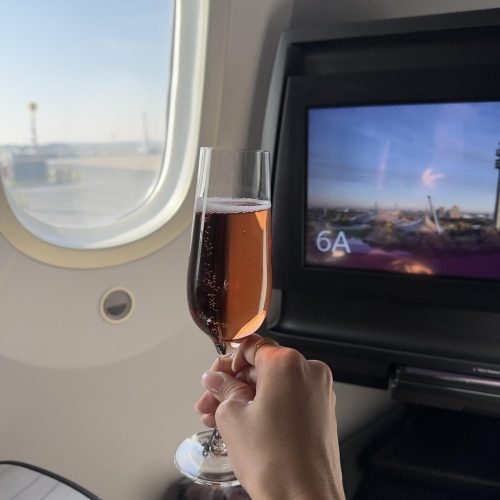 Rosé-Champagner im Glas vor einem Flugzeugfenster bei Sonnenschein – luxuriöser Reisemoment